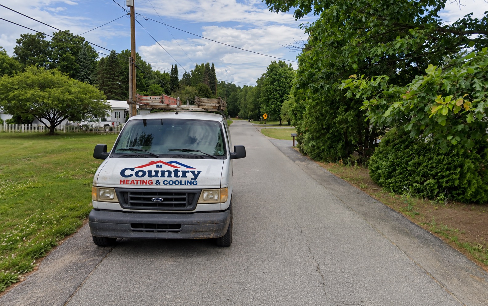 Country Heating & Cooling service van parked on a tree-lined residential street in Queensbury